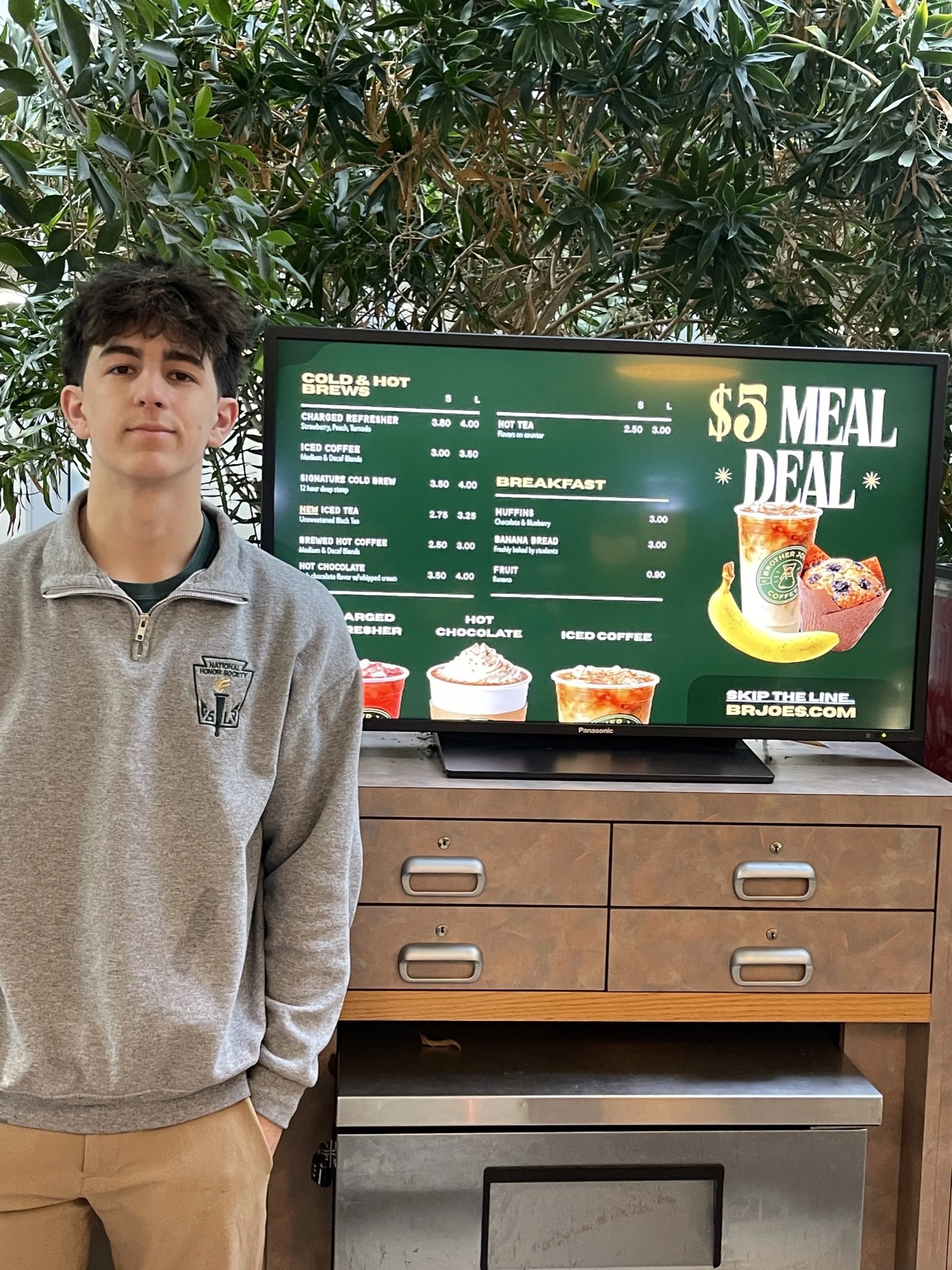 Rocco standing beside the Brother Joe's Coffee Co. menu board he built for his school