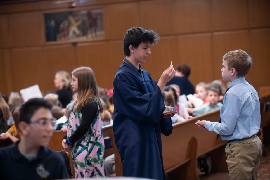 Rocco in a blue server's robe distributing communion to a young student at school mass