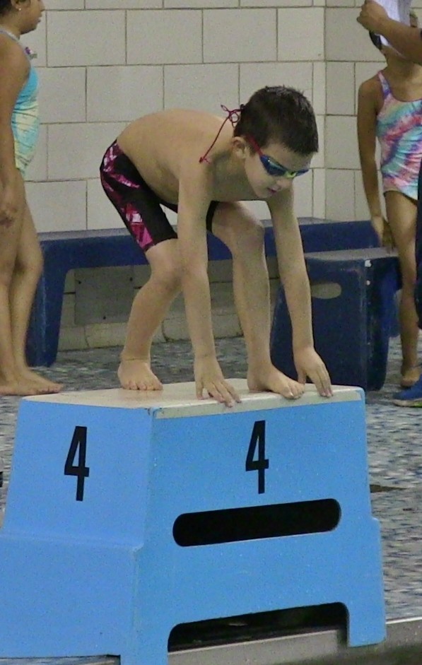 Young Rocco in goggles crouched on starting block number 4 at a swim meet